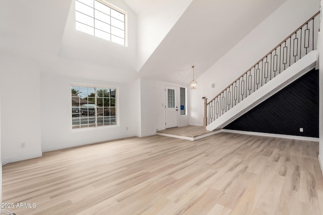 unfurnished living room with stairs, a high ceiling, and wood finished floors