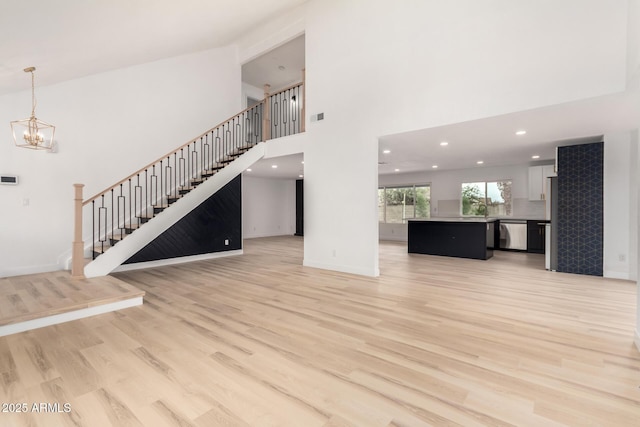 unfurnished living room with light wood finished floors, baseboards, a towering ceiling, stairway, and an inviting chandelier