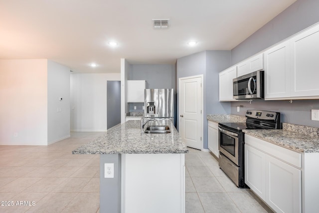 kitchen with an island with sink, white cabinetry, sink, stainless steel appliances, and light stone countertops