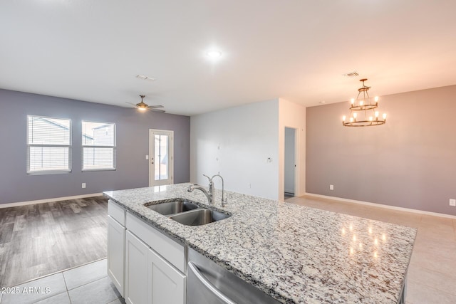 kitchen with sink, white cabinets, hanging light fixtures, a kitchen island with sink, and light stone countertops