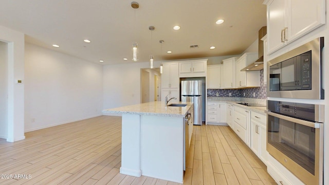kitchen featuring appliances with stainless steel finishes, an island with sink, a sink, and light wood finished floors
