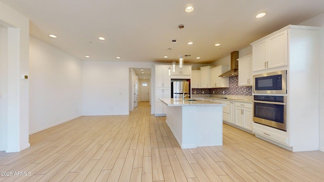 kitchen featuring appliances with stainless steel finishes, backsplash, light wood finished floors, and wall chimney exhaust hood