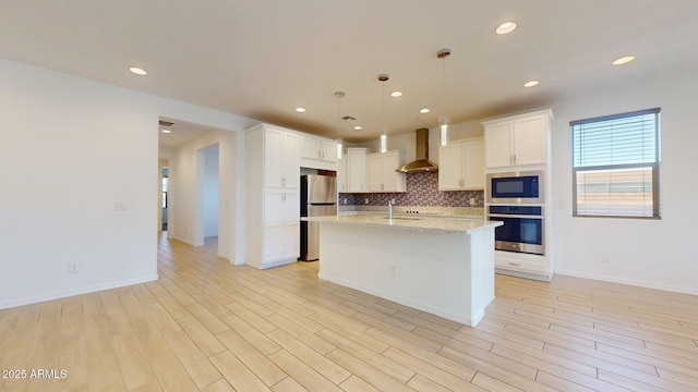 kitchen with wall chimney exhaust hood, white cabinets, tasteful backsplash, decorative light fixtures, and stainless steel appliances
