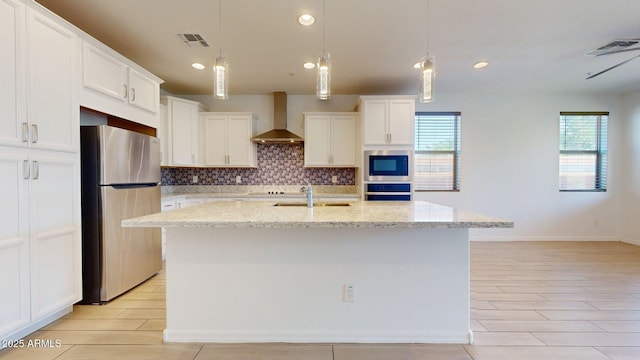 kitchen featuring wall chimney range hood, decorative backsplash, visible vents, a sink, and freestanding refrigerator