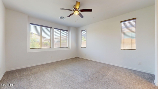 spare room featuring light colored carpet, a ceiling fan, visible vents, and baseboards