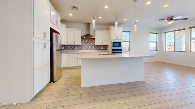 kitchen with visible vents, freestanding refrigerator, wall chimney exhaust hood, white cabinetry, and backsplash