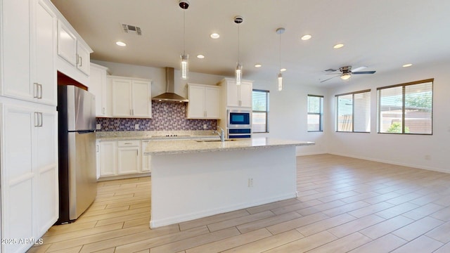 kitchen featuring visible vents, black electric cooktop, a sink, freestanding refrigerator, and wall chimney exhaust hood