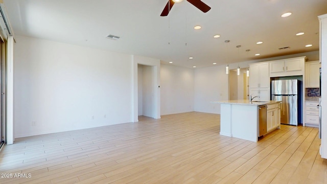 kitchen featuring visible vents, open floor plan, an island with sink, a ceiling fan, and appliances with stainless steel finishes