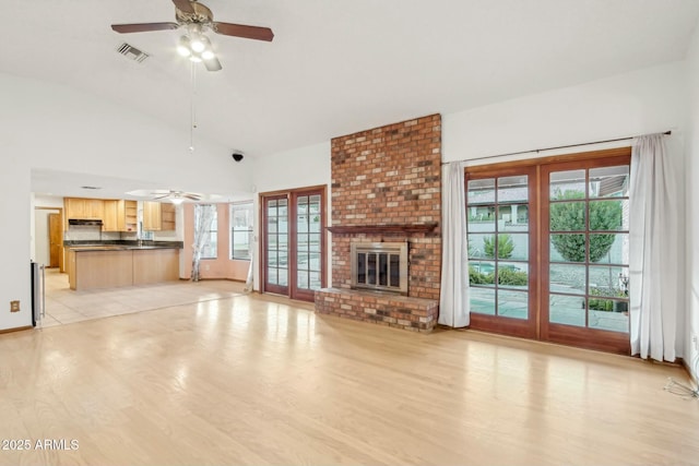 unfurnished living room with a brick fireplace, light hardwood / wood-style floors, french doors, and ceiling fan