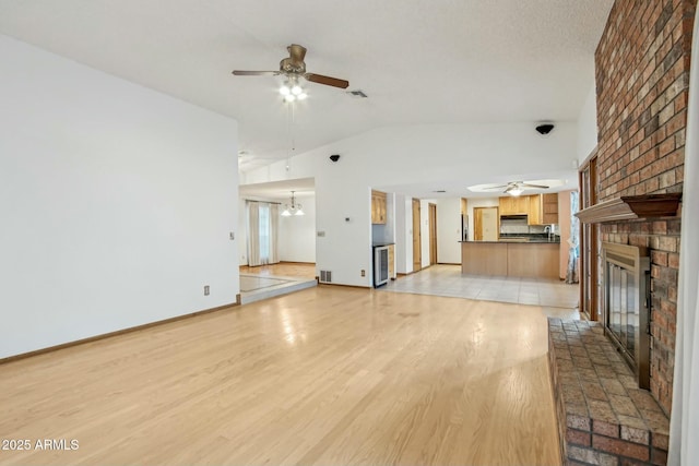 unfurnished living room with lofted ceiling, ceiling fan with notable chandelier, a fireplace, and light hardwood / wood-style flooring