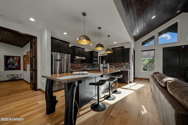 kitchen with high quality fridge, a kitchen island with sink, open floor plan, light countertops, and hanging light fixtures