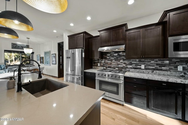 kitchen featuring premium appliances, backsplash, hanging light fixtures, under cabinet range hood, and a sink