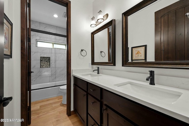 bathroom featuring toilet, combined bath / shower with glass door, a sink, and wood finished floors