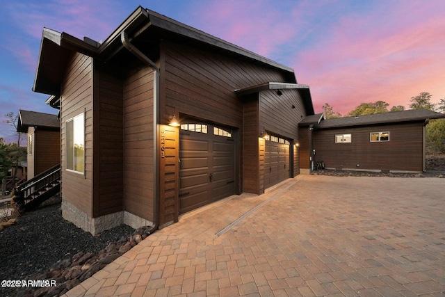 property exterior at dusk with a garage and decorative driveway