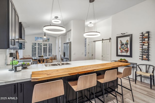 kitchen with a breakfast bar area, light wood-style flooring, a barn door, vaulted ceiling, and stainless steel fridge with ice dispenser