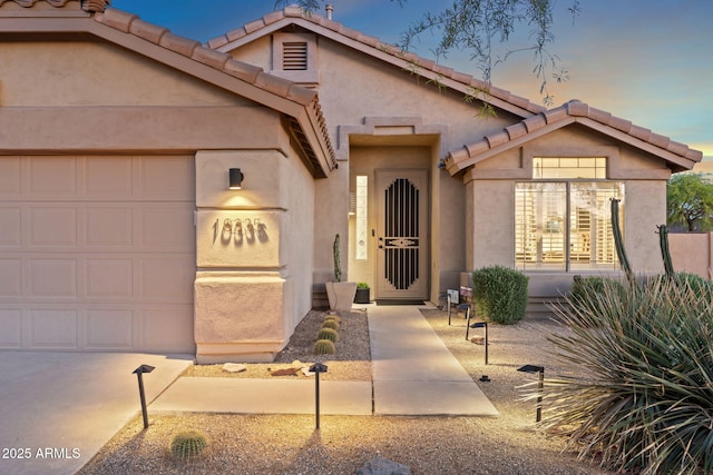 view of front facade featuring stucco siding, a tile roof, and an attached garage