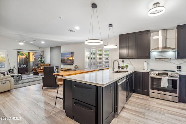 kitchen with light wood-style flooring, appliances with stainless steel finishes, a sink, visible vents, and wall chimney exhaust hood
