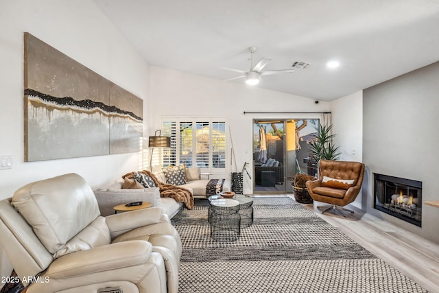 living room featuring visible vents, a glass covered fireplace, vaulted ceiling, wood finished floors, and a ceiling fan
