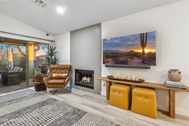 living room featuring visible vents, a lit fireplace, baseboards, light wood finished floors, and vaulted ceiling