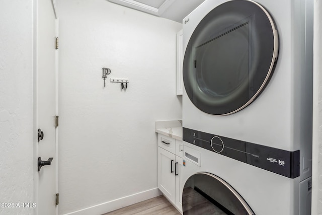 clothes washing area with baseboards, stacked washer and dryer, cabinet space, and light wood finished floors