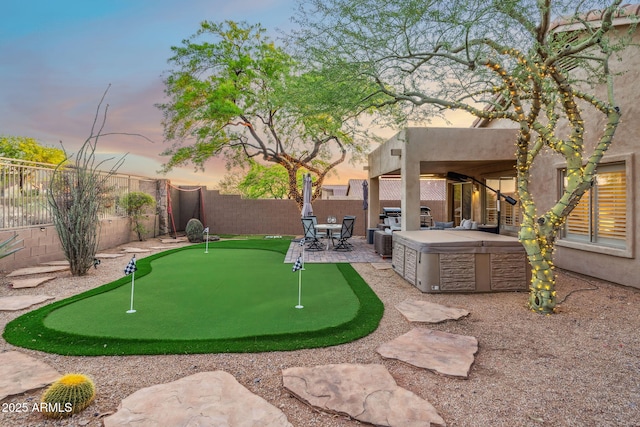 yard at dusk featuring a patio, a fenced backyard, and a hot tub