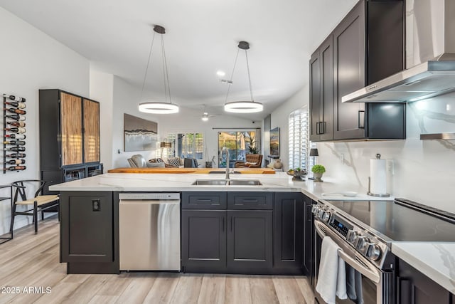 kitchen featuring a sink, stainless steel appliances, a peninsula, wall chimney range hood, and open floor plan