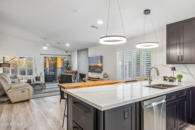 kitchen featuring stainless steel dishwasher, a sink, open floor plan, light wood finished floors, and vaulted ceiling