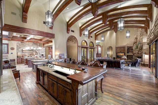 kitchen featuring high vaulted ceiling, dark wood-type flooring, a fireplace, and an island with sink