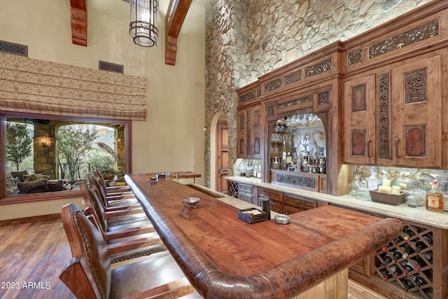 bar with pendant lighting, hardwood / wood-style floors, tasteful backsplash, beam ceiling, and a towering ceiling