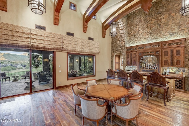 dining space featuring light hardwood / wood-style floors, high vaulted ceiling, beam ceiling, a mountain view, and bar