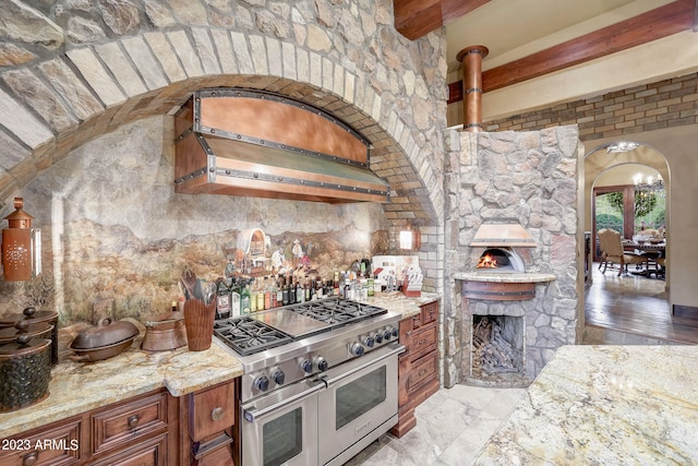 kitchen featuring double oven range, light stone countertops, wall chimney exhaust hood, a fireplace, and light tile flooring