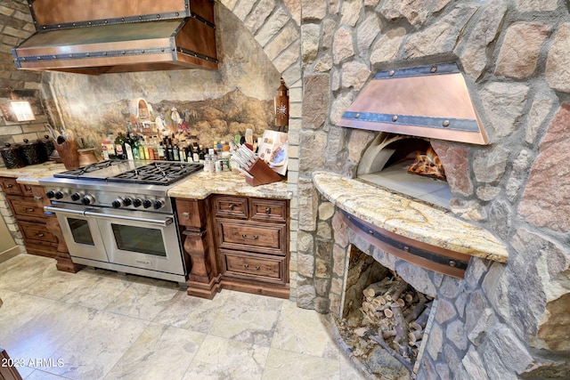 kitchen featuring double oven range, wall chimney range hood, and light tile floors