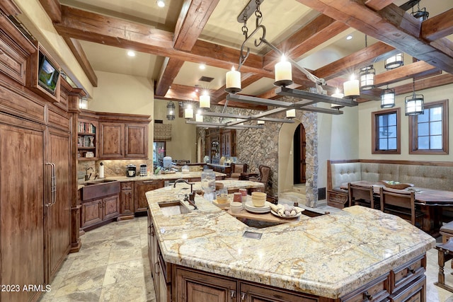 kitchen featuring an island with sink, sink, light stone countertops, and beamed ceiling