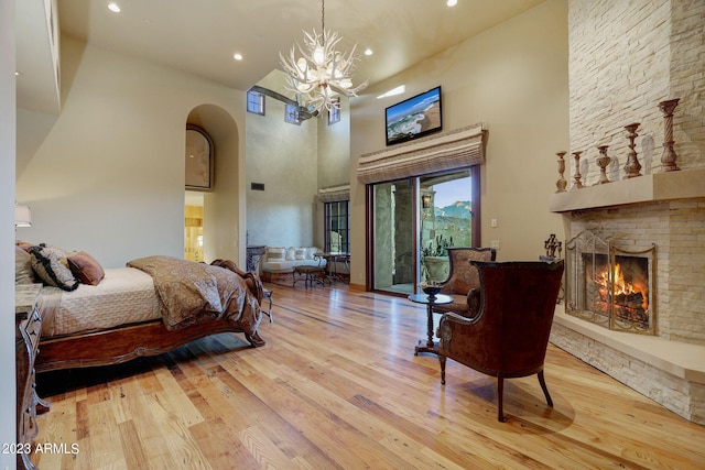 bedroom featuring a notable chandelier, a stone fireplace, a towering ceiling, access to outside, and light wood-type flooring