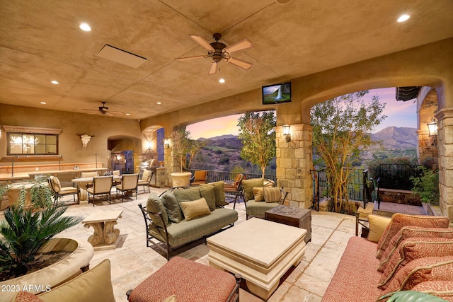 patio terrace at dusk with ceiling fan, an outdoor hangout area, and a mountain view