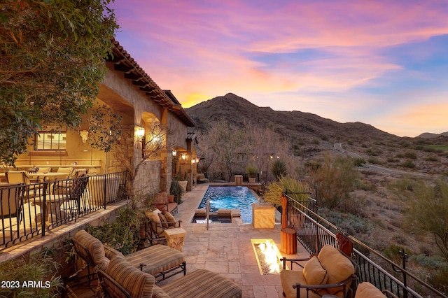 patio terrace at dusk with pool water feature, a mountain view, and a fenced in pool