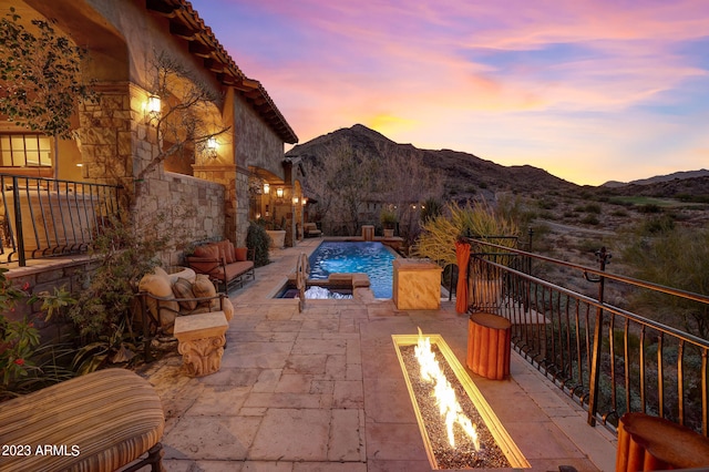 patio terrace at dusk featuring an outdoor fire pit, a mountain view, a fenced in pool, and pool water feature