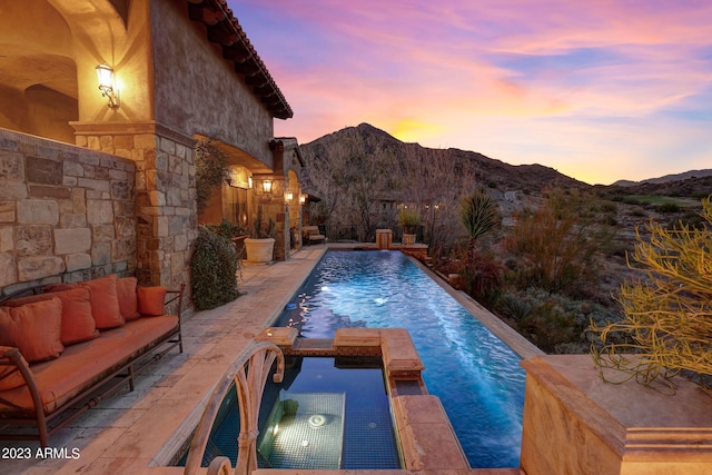 pool at dusk featuring a mountain view, a patio, an in ground hot tub, and pool water feature