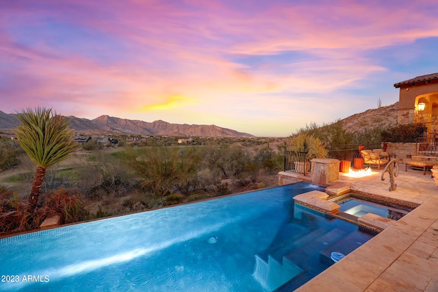 pool at dusk with a mountain view, an in ground hot tub, a fire pit, and a patio