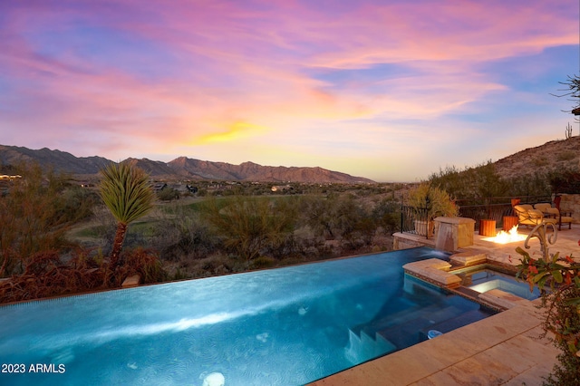 pool at dusk featuring a mountain view and an in ground hot tub