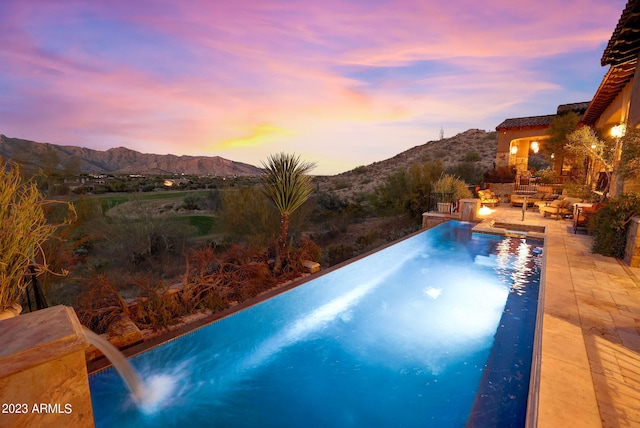 pool at dusk with a patio area, pool water feature, and a mountain view