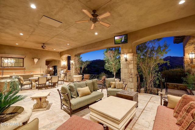 patio terrace at twilight featuring a mountain view, an outdoor living space with a fireplace, and ceiling fan