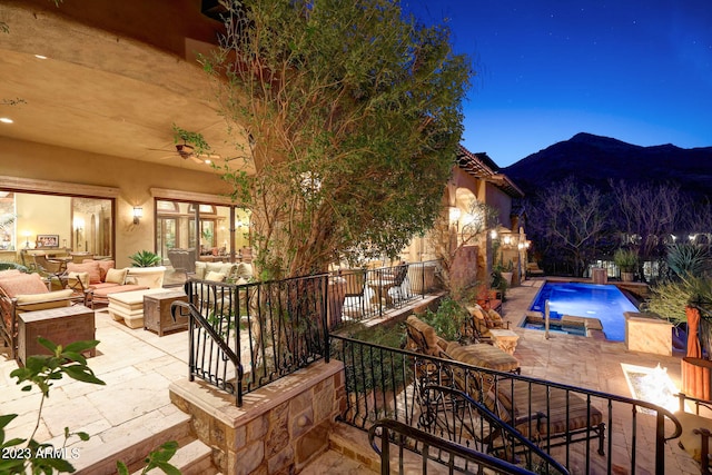 patio terrace at night featuring an outdoor hangout area, a fenced in pool, a mountain view, and pool water feature