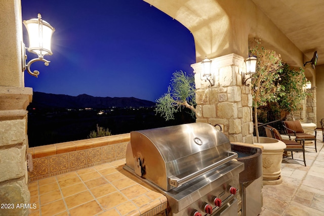 patio terrace at night featuring a mountain view, area for grilling, and a grill