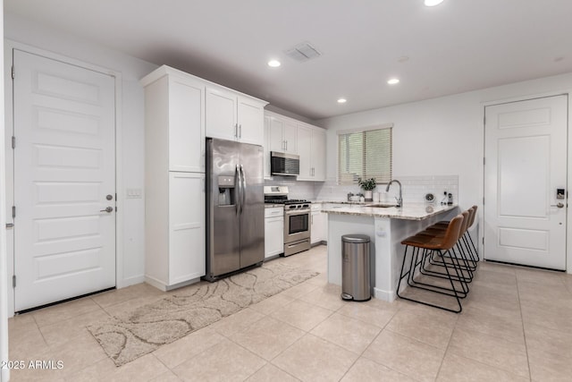 5897 N 195th Dr, Litchfield Park, AZ 85340 - kitchen with appliances with stainless steel finishes, a sink, a peninsula, white cabinetry, and a kitchen bar