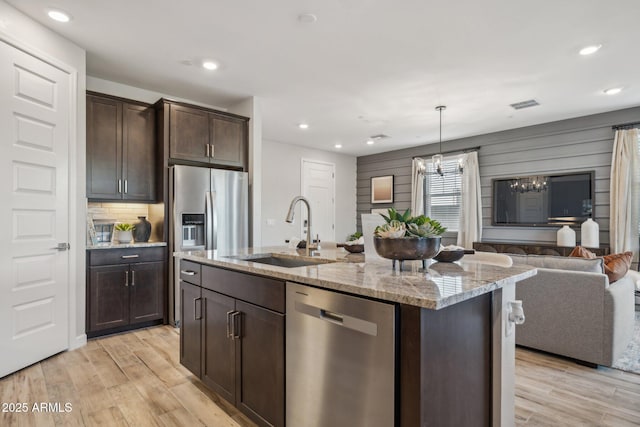 kitchen featuring sink, dark brown cabinets, appliances with stainless steel finishes, an island with sink, and light stone countertops