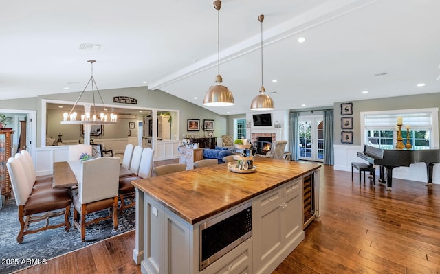 kitchen with stainless steel microwave, a fireplace, hanging light fixtures, a kitchen island, and white cabinets