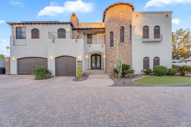 mediterranean / spanish home with a balcony, stucco siding, french doors, stone siding, and decorative driveway