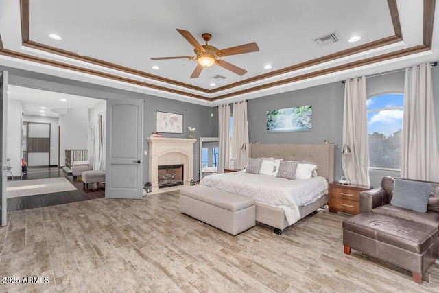 bedroom with crown molding, a fireplace, light wood-type flooring, visible vents, and a raised ceiling