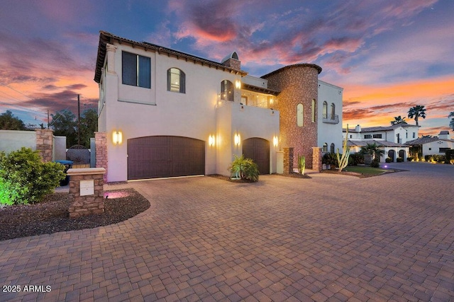 mediterranean / spanish house featuring a garage, stucco siding, and decorative driveway